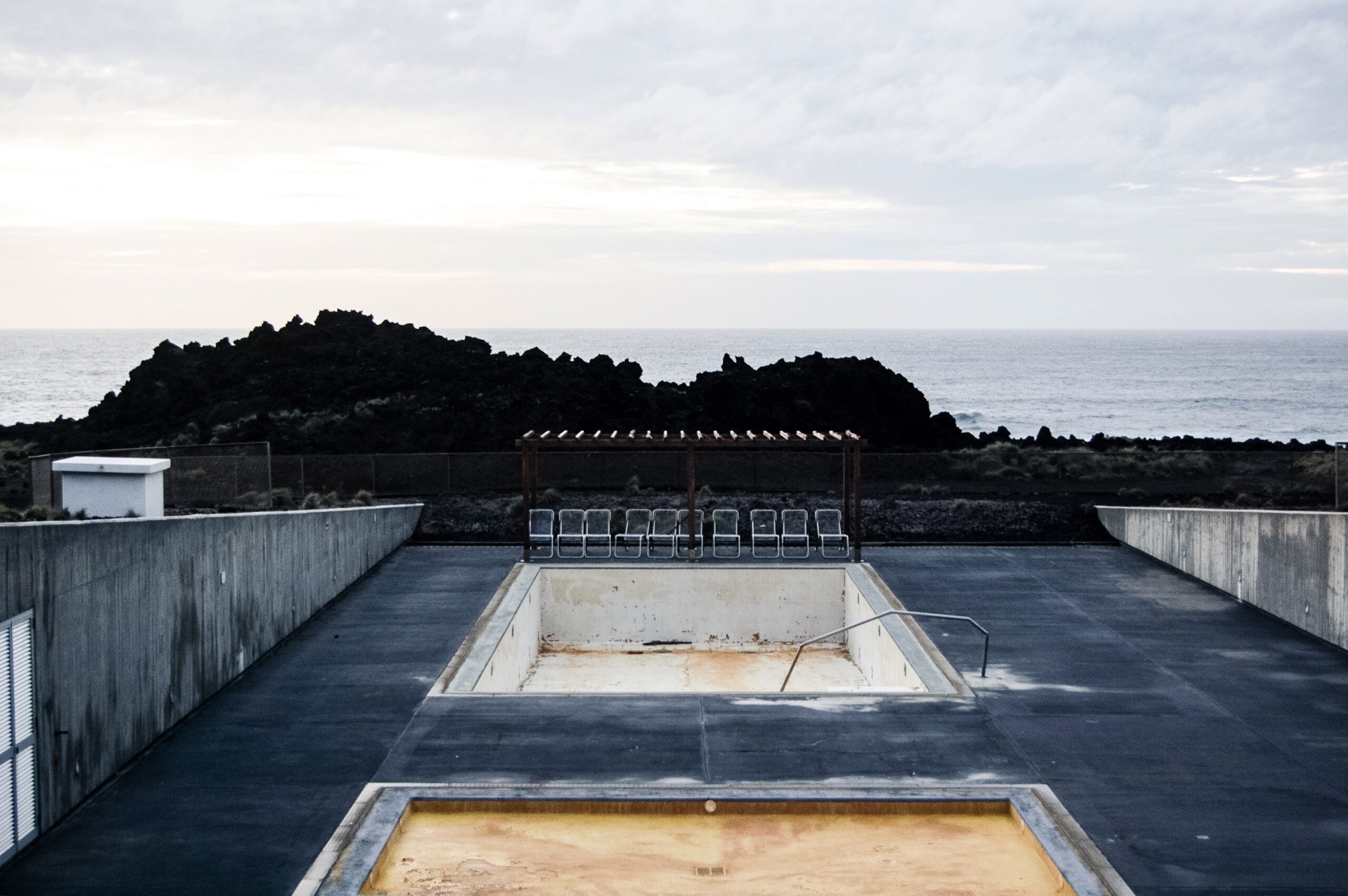 An empty pool with chairs  near the cliff and a sea